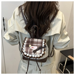 Détail du sac à dos avec rabat à carreaux marron, bordure en dentelle et nœud chic