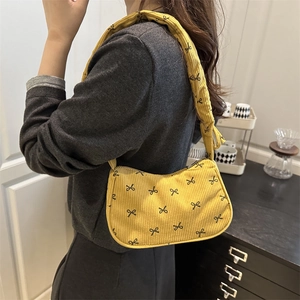 Sac sous le bras en velours côtelé jaune avec nœuds noirs porté par un mannequin