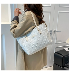 Close-up of a white tote bag with embossed texture and metal logo detail on a model