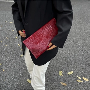 Rote Clutch mit Krokodilmuster und Glanz-Finish, getragen von Model im Anzug