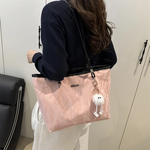 Pink textured tote bag with black handles and white pompom pendant shown on shoulder