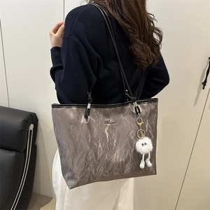 Silver metallic pleated tote bag with plush charm shown in a minimalist studio setting