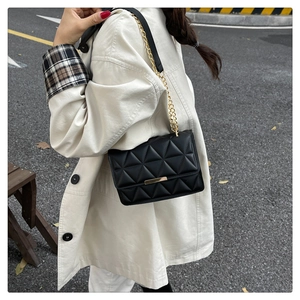 Dettaglio borsa trapuntata nera con fibbia dorata indossata su un cappotto beige
