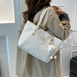 White bohemian tote bag with quilted texture and cloud pendant worn with a trench coat