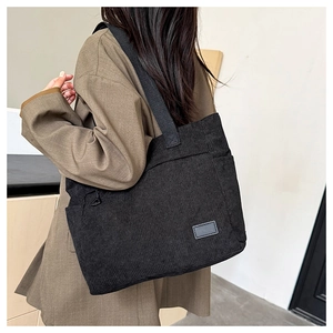 Detalle del bolso tote de pana negra con textura acanalada y bolsillo lateral puesto
