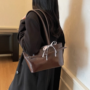 Deep brown minimalist tote bag with metal ring and decorative ribbon on woman's shoulder