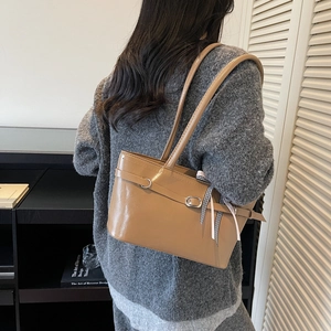 Minimalist brown leather shoulder bag with decorative ribbon shown on a model