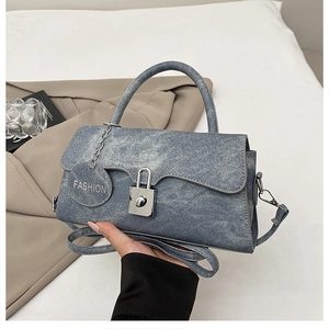 Dettaglio di borsa in denim azzurro con chiusura in argento e ciondolo alla moda