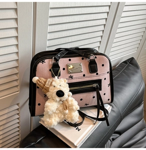 Detail view of pink polka dot bag with black leather trim and white teddy bear charm