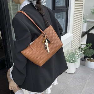 Brown woven leather tote bag with vintage bead charm worn by a model on a shoulder