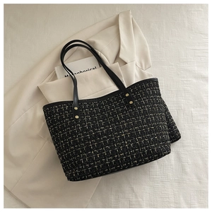Close-up of black tweed tote bag with gold metal buckles on textured cream surface