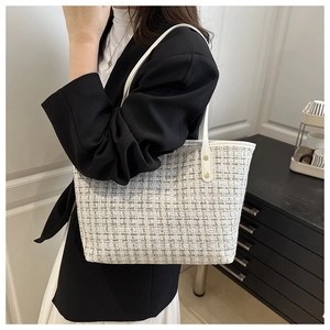 Detail of tweed tote bag with gold rivets and leather strap on a black blazer