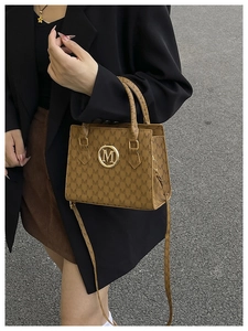 Detail of brown monogram tote bag with gold M logo and adjustable shoulder strap on model