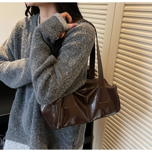 Detailed view of deep brown patent leather tote bag styled with a grey knitted sweater