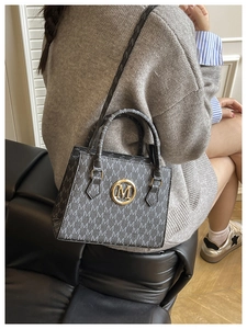 Close-up of a grey leather crossbody bag with M-letter pattern and gold metal logo