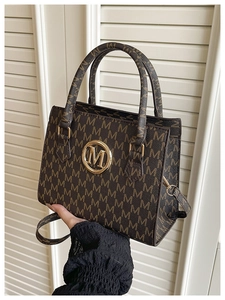 Detail of dark brown monogram handbag with gold M logo and textured synthetic leather