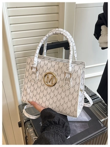 Detail of white tote bag featuring M-letter print and golden circular metal logo