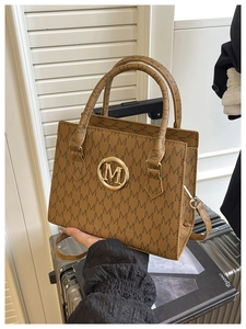 Detailed close-up of brown textured crossbody bag featuring vintage M letter pattern and logo