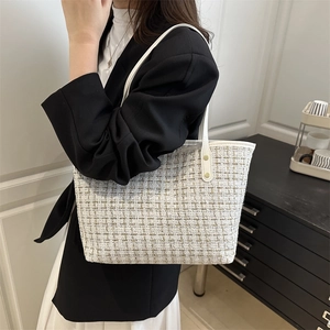 White tweed tote bag with leather handles and gold studs worn by a model in a suit
