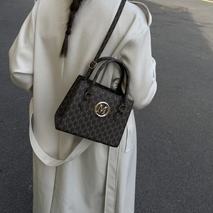 Brown monogram tote bag with gold M buckle, shown outdoors with a stylish beige trench coat