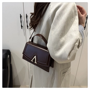 Détail d'un sac bandoulière marron foncé avec un fermoir en métal doré en forme de V