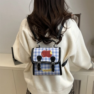 Blue gingham mini backpack with apple graphic worn over a beige sweater in a cozy room