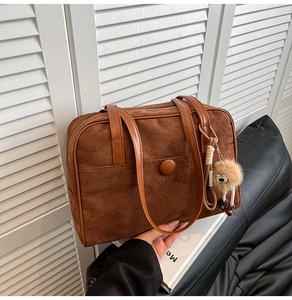 Detail of vintage brown suede tote bag featuring a decorative buckle and plush charm