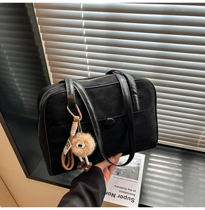 Detailed view of black suede shoulder bag with plush monster charm and front pocket