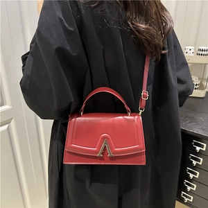 Sac bandoulière en cuir rouge minimaliste avec fermoir doré en V sur une tenue noire