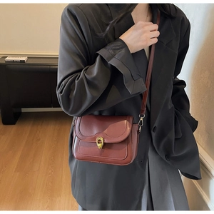 Detail of vintage dark red leather crossbody bag with iconic gold circular hardware buckle