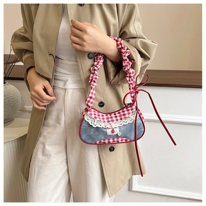 Detail of denim and red plaid bag with cherry patch and white lace edges worn by model