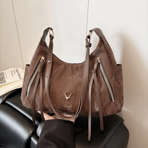 Détail d'un sac cabas marron foncé à texture plissée, ornement cerf et glands latéraux