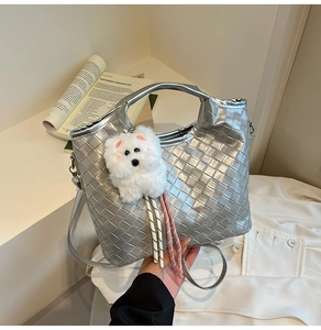 Detail of silver woven handbag with white plush dog pendant and crossbody strap
