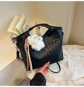 Detail of black woven leather handbag with plush animal charm and colorful rope accent