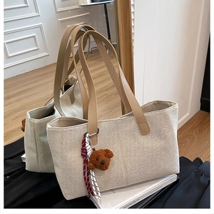 Detail of canvas tote bag with brown leather handles and a plush bear pendant accessory