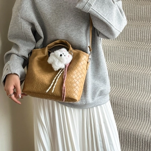 Caramel woven bucket bag with teddy bear charm on model in gray sweater and white skirt
