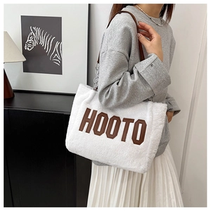 Primer plano del bolso tote de felpa blanca con letras HOOTO y correa de cadena marrón