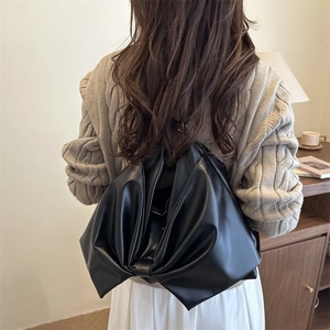 Minimalist black leather bow shoulder bag for women shown on a model in a home setting