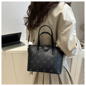 Close-up of black leather tote with vintage logo print and stylish brown wide fabric strap