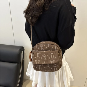 Brown corduroy crossbody bag with white bow patterns worn by a girl on a black sofa