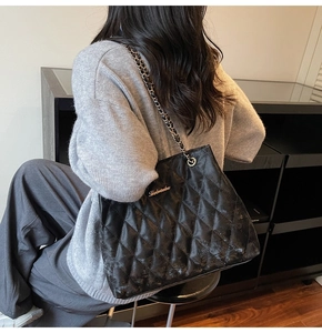 Detail of black quilted tote bag with golden metal logo and elegant chain strap