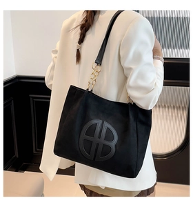 Detalle de un bolso tote de ante negro con parche de logo y correa de cadena dorada