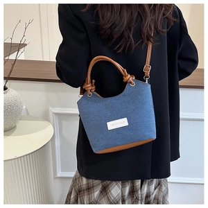 Détail du sac seau en denim avec lanières en cuir marron porté par un mannequin en salle