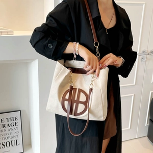 Bolso tote grande de lona beige con detalles de cuero marrón y cadena en modelo