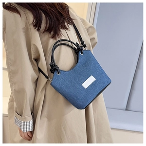 Sac seau en jean bleu avec poignées rondes noires et bandoulière sur un trench