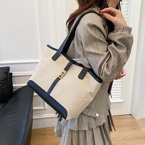 Minimalist canvas tote bag with black leather trim and metal lock shown on a model shoulder