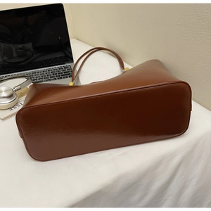 Close-up of brown glossy leather tote bag bottom with neat stitching and work accessories