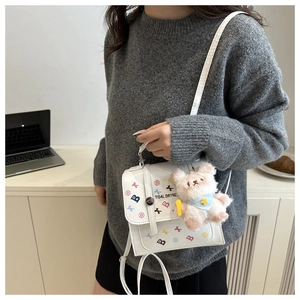 Détail d'un mini sac blanc avec des imprimés graphiques et un porte-clé ours peluche