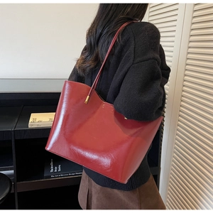 Detailed side view of a large burgundy patent leather tote bag with thin shoulder straps