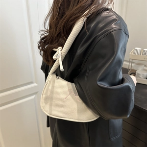 Sac à bandoulière en velours côtelé beige avec broderie de nœud rose porté par un mannequin